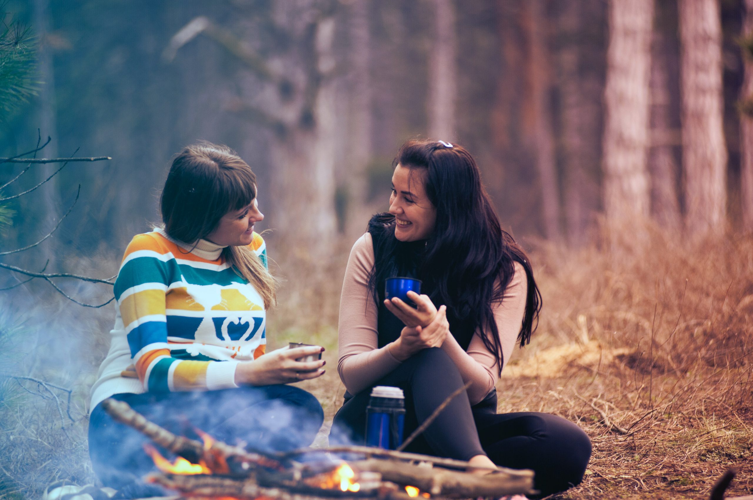 Par de amigas conversando en medio del bosque con un café en la mano